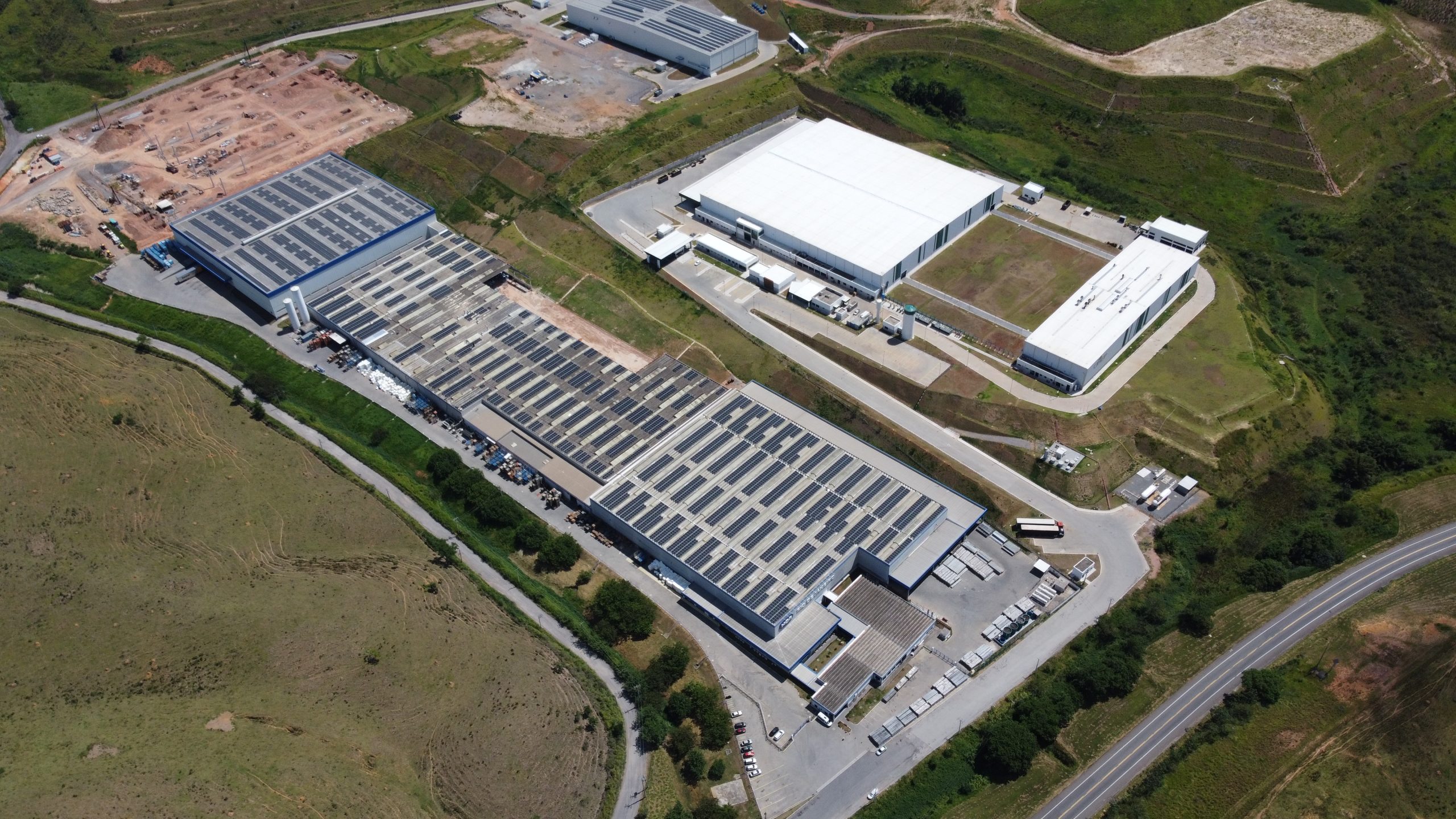 Vista aérea de complexo industrial com painéis solares fotovoltaicos instalados nos telhados dos galpões.